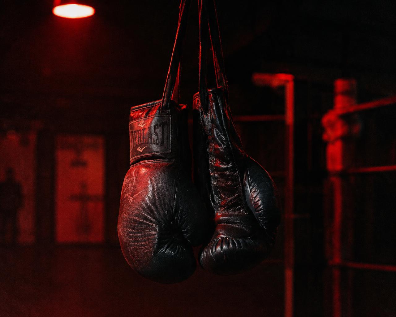 A pair of worn boxing gloves hanging in a dim gym